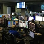 A bustling control room with people working on multiple computer monitors.